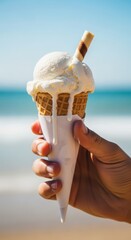 A hand holding a melting vanilla ice cream cone with a wafer stick on a sunny beach with the ocean in the background