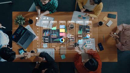 A diverse business team gathers around a table sharing insights on data analysis, with visuals of charts and graphs displayed digitally, emphasizing teamwork and strategy. Trope