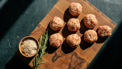 Raw meatballs on a wooden board with herbs and spices, ready for cooking.