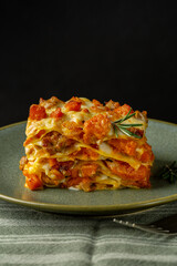 Green plate with Pumpkin, cheese and sausage lasagna. Italian Baked pasta, homemade food. Close up. Black background. Vertical image.