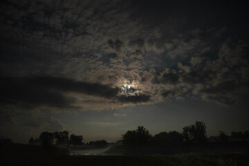 Moonlight breaking through clouds over river landscape
