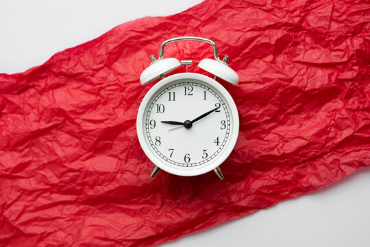 Alarm clock on red backdrop symbolizes menstruation cycle