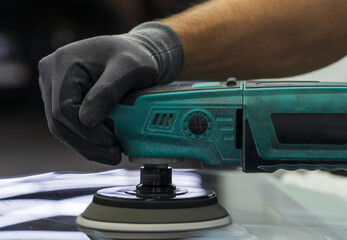 A man polishes the glass of a car with a polishing machine from small scratches with a large one. Auto glass repair, replacement. Car detailing. Hands with an orbital polishing machine. Close-up.