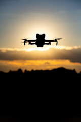 Silhouette of a Drone Flying in the Sky at Sunset with Glowing Sunlight and Scenic Cloudscape in the Background