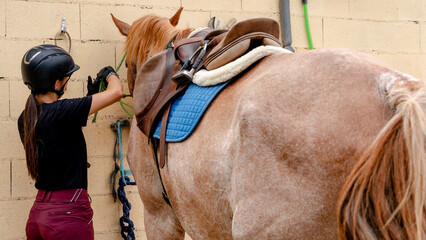 Young rider tying saddled horse to wall at equestrian centre