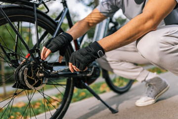 Naklejka premium Young man fixes bicycle chain, concept of bike maintenance, repair, cycling, outdoor activity, urban mobility, healthy lifestyle, cycling mechanic.