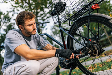 Obraz premium Young man fixes bicycle chain, concept of bike maintenance, repair, cycling, outdoor activity, urban mobility, healthy lifestyle, cycling mechanic.