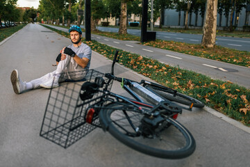 Young man fallen from bicycle lying on sidewalk with helmet