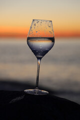 1 one alone transparent glass of white wine on yellow sunset beach at colorful sundown. glass with water, wine above sun set Black sea or ocean. Batumi, Georgia. evening time night scene Summer season