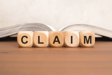 Wooden blocks with CLAIM word on wooden desk with open book background