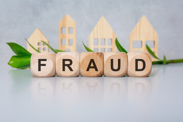 wooden cubes with black letters spelling FRAUD on white table with green leaves and house models