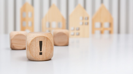 Wooden cube with exclamation mark on financial sheet before wooden house models
