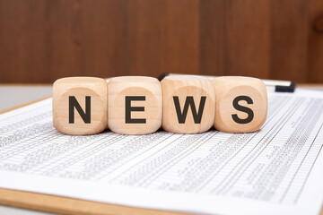 wooden cubes with black letters NEWS on financial spreadsheet and wooden background