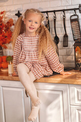 Cute little girl in a plaid dress sitting and posing on a rustic kitchen countertop decorated for autumn, with a happy and cheerful expression. autumn season,  autumn concept,  fall