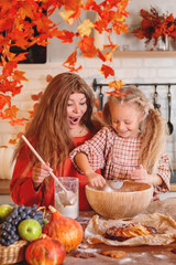 Happy mother and daughter baking together, rolling out dough in a flour-dusted, autumn-themed rustic kitchen with a harvest of fruit and pumpkins. autumn season,  autumn concept,  fall. Halloween. 
