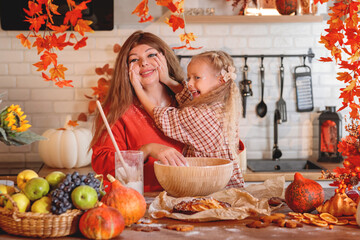 Happy mother and daughter baking together, rolling out dough in a flour-dusted, autumn-themed rustic kitchen with a harvest of fruit and pumpkins. autumn season,  autumn concept,  fall. Halloween. 