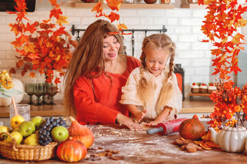 Happy mother and daughter baking together, rolling out dough in a flour-dusted, autumn-themed rustic kitchen with a harvest of fruit and pumpkins. autumn season,  autumn concept,  fall. Halloween. 
