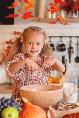 autumn still life. Happy little girl playing with dough and baking a pie in a rustic kitchen full of autumn harvest decorations, including pumpkins, fruit, and fall leaves. autumn season.