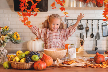 autumn still life. Happy little girl playing with dough and baking a pie in a rustic kitchen full of autumn harvest decorations, including pumpkins, fruit, and fall leaves. autumn season.