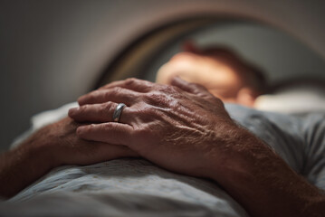 Close-up of patient’s nervous hands gripping blanket inside scanner.
