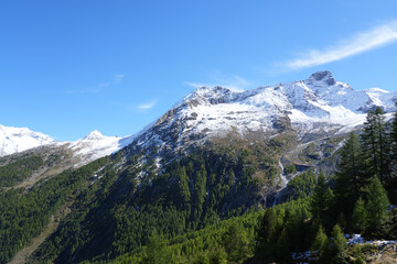 Majestic snow-capped mountains rise above lush green valleys under a clear blue sky, showcasing the beauty of nature and the tranquility of the alpine landscape