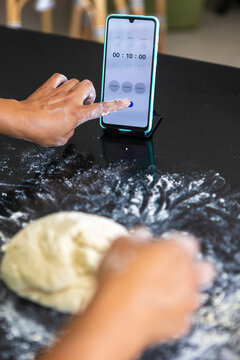 Woman preparing dough with smartphone timer in kitchen