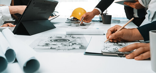A diverse team gathers in a modern office to collaborate on engineering designs, discussing project blueprints with tools, documenting ideas, and strategizing. SACTR