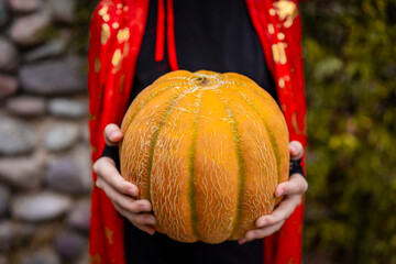 Girl holding pumpkin in Halloween costume with red cape