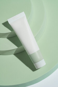 White cosmetic tube on green podium from above