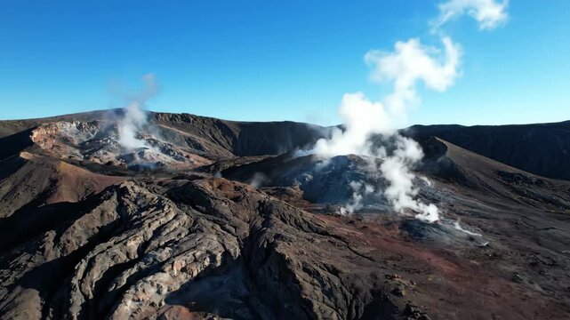 Drone shot slowly descends over a rugged volcanic landscape, showcasing steaming fumaroles and unique geological formations under a clear sky clear sky, adventure, rock