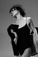 Fototapeta premium Black and white portrait of a stylish woman wearing sunglasses and a swimsuit with a jacket in a minimalistic setting.
