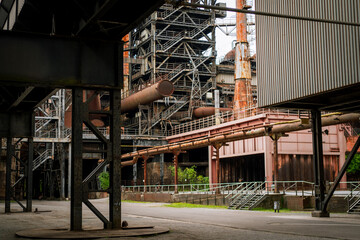 Abandoned industrial factory with rusty pipes, steel structures, and metal staircases. Urban exploration scene with decay, textures, and overgrown vegetation in a post-industrial setting.