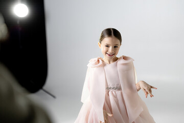 A young girl in a flowing pink dress sits on the floor with her legs extended and head down.