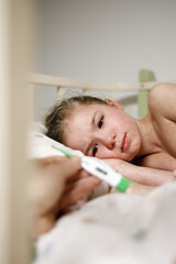 a photo of an electronic thermometer in the hands of a parent measuring the body temperature of their child, fever in a sick child