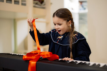 A young girl excitedly opens a gift-wrapped electronic keyboard with a red ribbon.