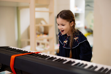 A young girl playing the piano while another person takes a photo with a smartphone.