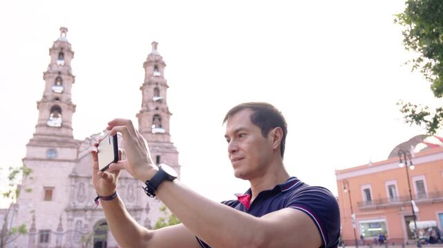 Young Hispanic Man Using Smartphone in front of Catedral Bas&iacute;lica of Our Lady of the Assumption in  Patria Plaza, Aguascalientes, Mexico. 