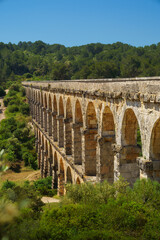 Obraz premium Aqüeducte de les Ferreres, a roman aqueduct, spanning Barranc de les Arcs near Tarragona, sunlit limestone arches and clear blue sky, ancient engineering heritage; ideal for travel ads