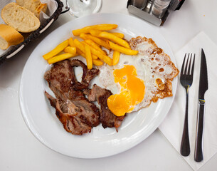 Cooked tender veal with fried egg and French fries. Serving a Spanish meat dish on a white plate
