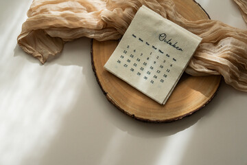Top view of linen fabric calendar with October month, sheer fabric, wooden slice, light background, copy space, aesthetic soft shadows	