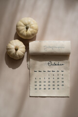 Linen fabric calendar with October month, decorative pumpkins, soft shadows, beige background, top view autumn aesthetic	