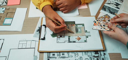 Close-up view of hands engaged in a collaborative design project showcasing sketches and color...
