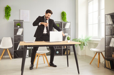 Young expressive businessman in formal suit dancing during break at workplace, singing song, having fun alone in modern office, distracted from workflow on laptop. Passion, hobby, rest during workday
