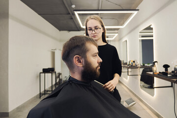 Professional woman barber wielding electric hair clipper making Fashionable haircut. Bearded Man client visit gentleman grooming beauty salon for hairstyle care. Modern Haircut style in barber shop