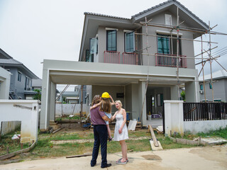 Family consist father mother daughter visit new construction two-story house. pointing at different part building expressing excitement anticipation for their future home. indicat ongoing construction