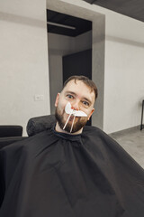 Barber removing hair in nose by waxing from Bearded Man face in stylish barbershop. Beautician hair removal procedure in male beauty salon. Male skin care and beard style concept