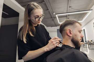 Professional barber wielding electric hair clipper making Fashionable haircut. Bearded Man client visit gentleman grooming beauty salon for hairstyle care. Modern Haircut style in barber shop close up