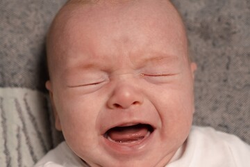 Little two month old newborn baby boy is crying. Screaming hungry infant face portrait close up. Baby experiences pain during colic in the abdomen