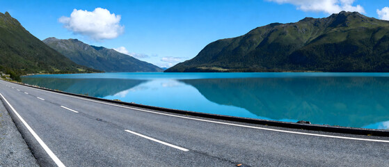 A scenic road alongside a clear blue lake with mountainous backdrop, showcasing natural beauty and serene environment.