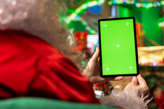 Santa Claus using green screen digital tablet to arrange delivery routes for Christmas Eve. Man in Santa costume plots winter holidays event journey to children houses using mockup touchscreen device